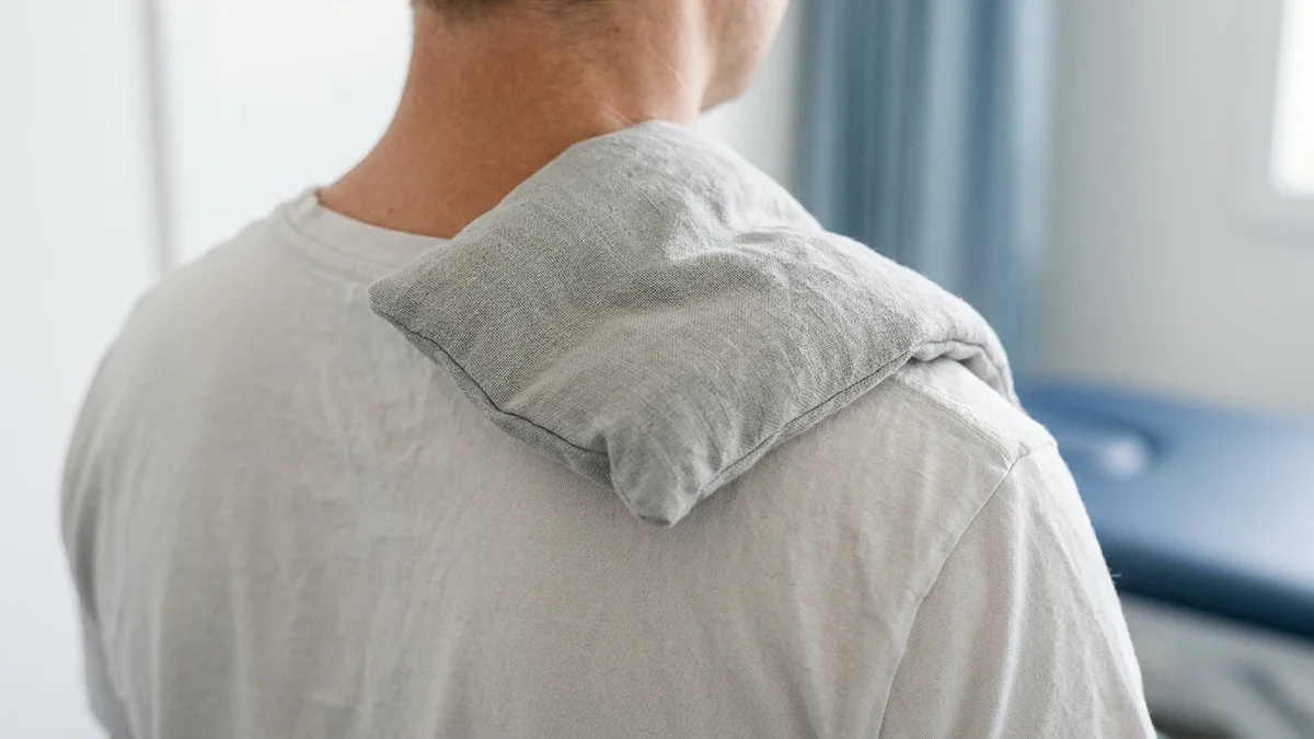 Wrapped heat pack resting on the back of the neck and top of the shoulder