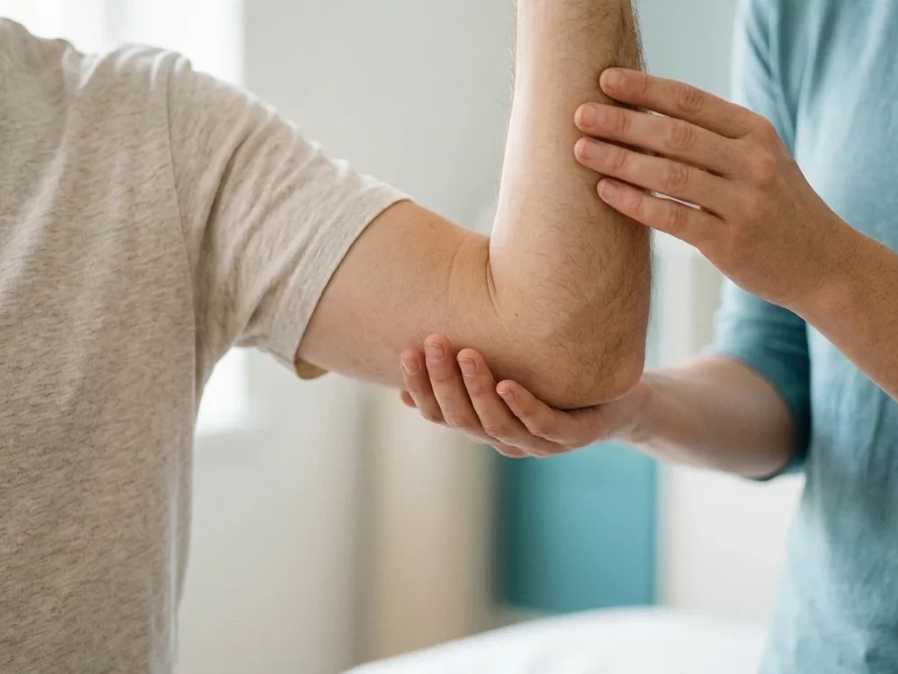 Physiotherapist's hands guiding a person's arm lift to shoulder height
